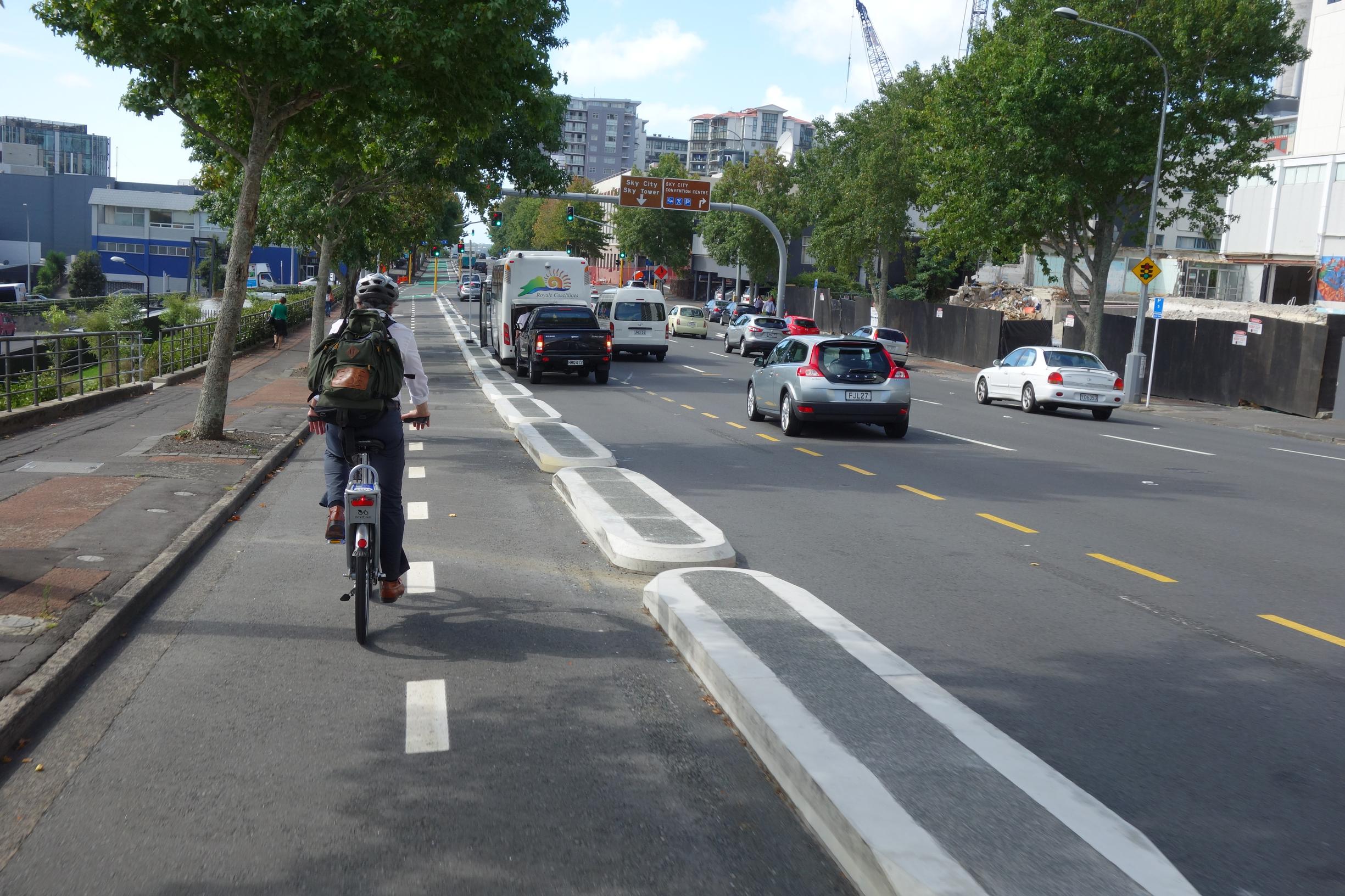 Cycling in Auckland is represented by new separated bikeway infrastructure largely added in the 2010s, such as the Lightpath / Nelson Street cycleway into the City Centre, which are credited with being part of the reason cycling counters have experienced large annual growth over the last years. Image courtesy Schwede66 CC