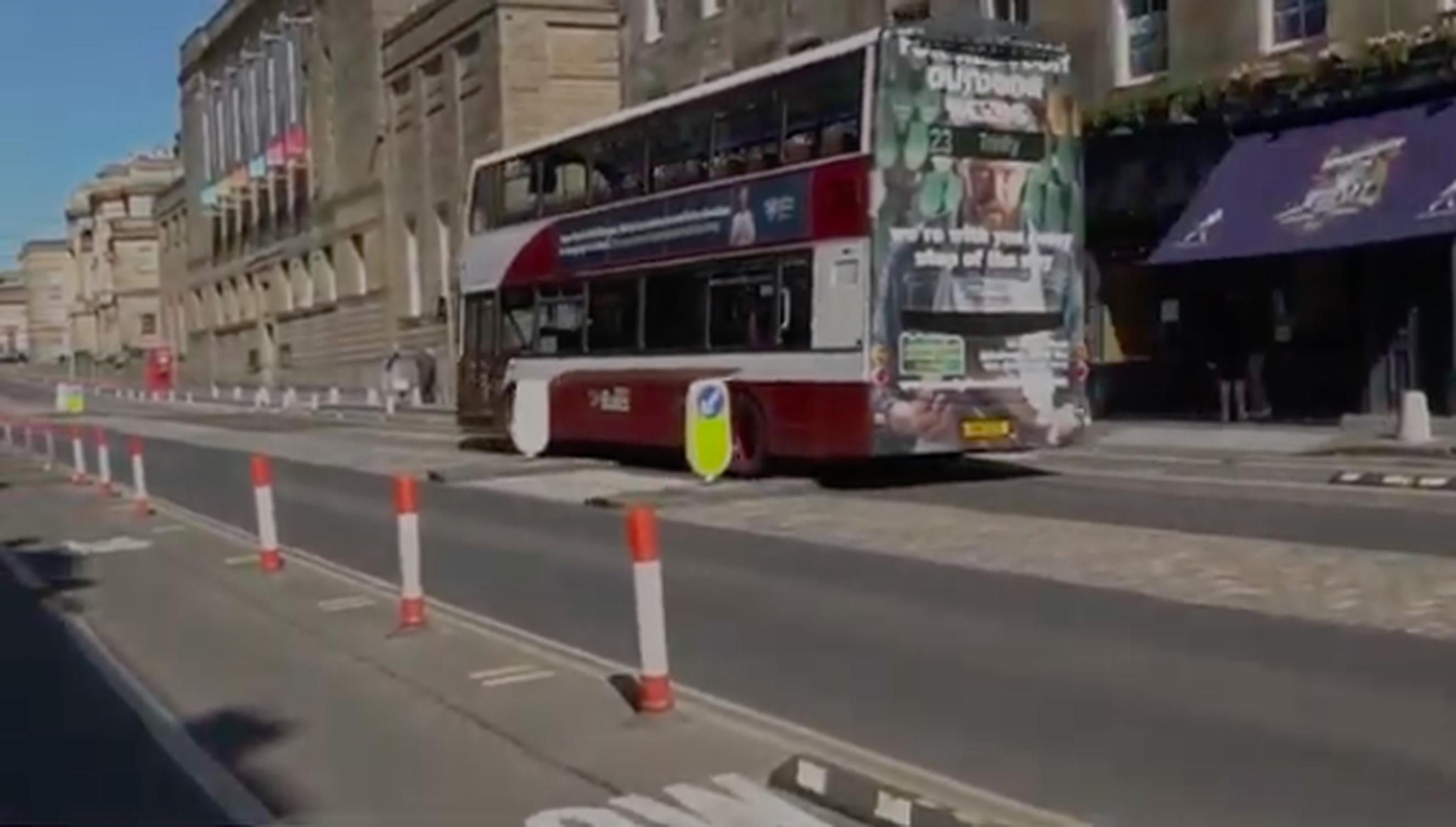 The video records a bus driving down the wrong side of a pedestrian refuge island to overtake the parked taxi