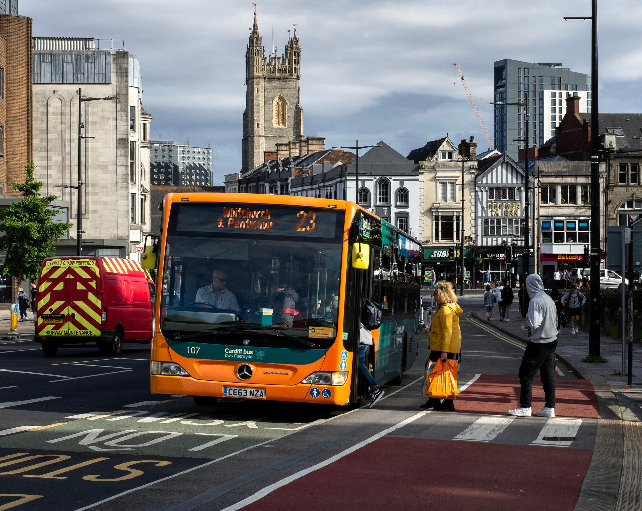 Passengers queue on a cycle track in front of a bus stop in Cardiff